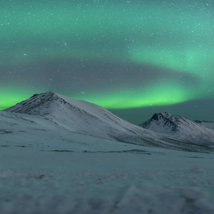 Bright, neon lights swirl in the starry night sky above a barren landscape of snowy mountains