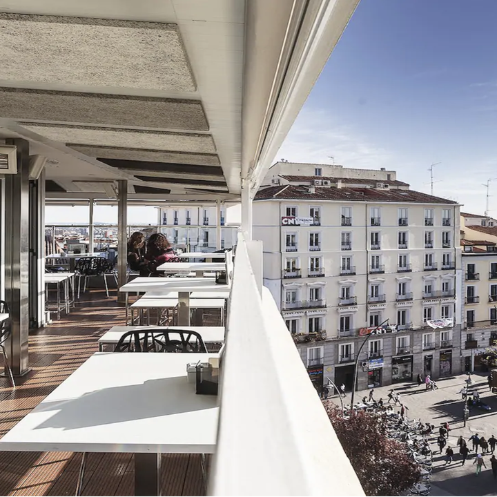 A view of a Spanish café upper floor patio with white tables and a view of the street below
