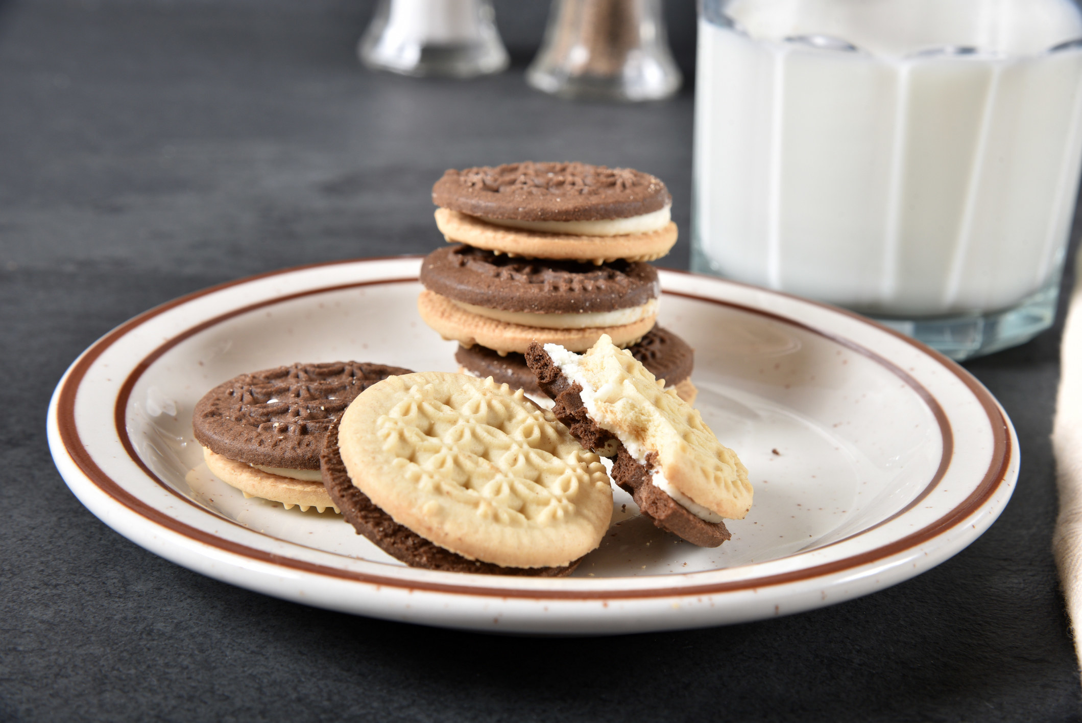 A stack of vanilla and chocolate sandwich cookies on plate next to a glass of milk