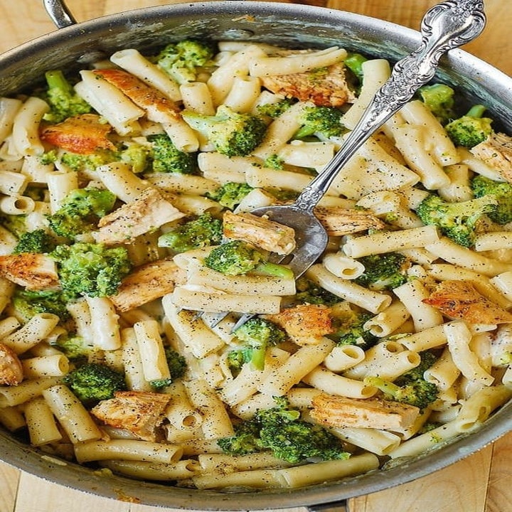 Pasta with chicken and broccoli all mixed together in a big pot.
