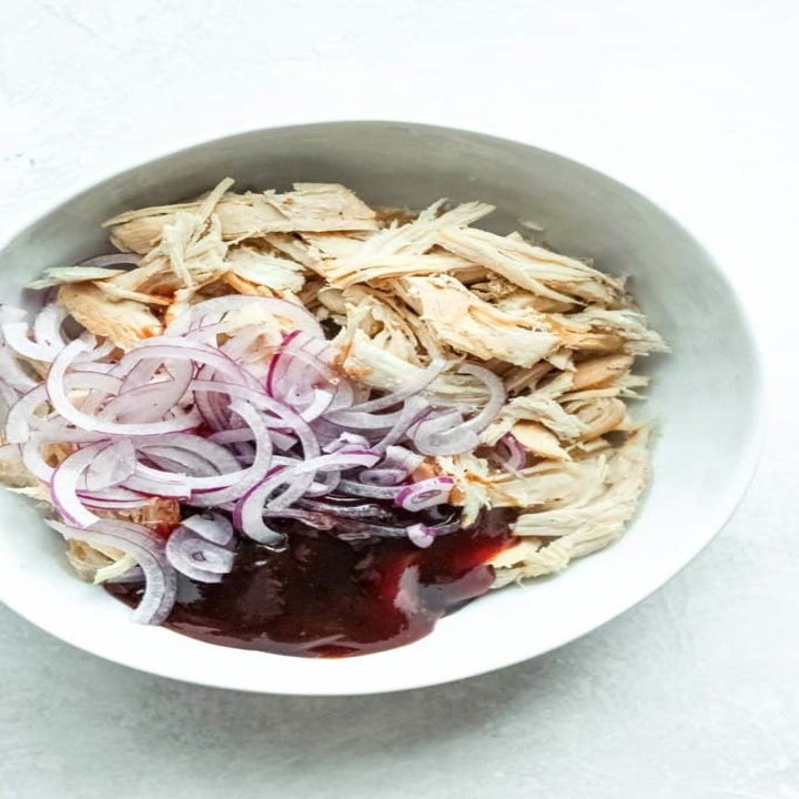 Shredded chicken, red onions, and barbecue sauce in a mixing bowl.