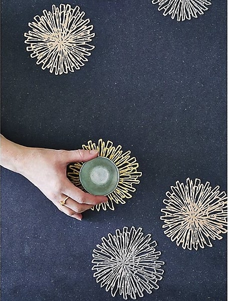 Four gold flower-like coasters with a hand setting a small glass on one