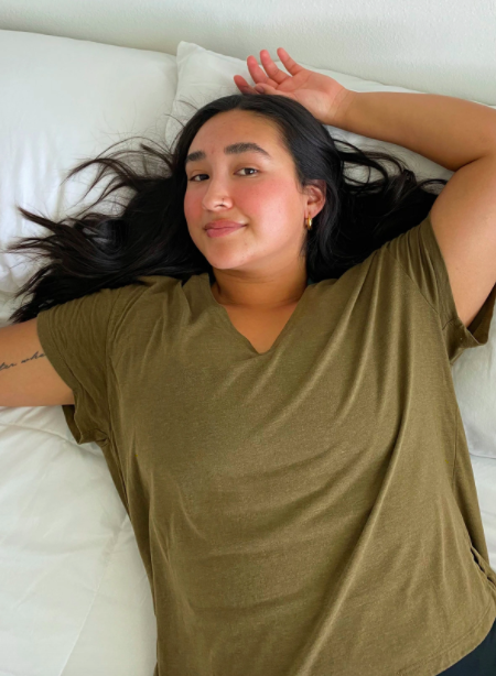 Model wears green v-neck tee while lounging on a white bed