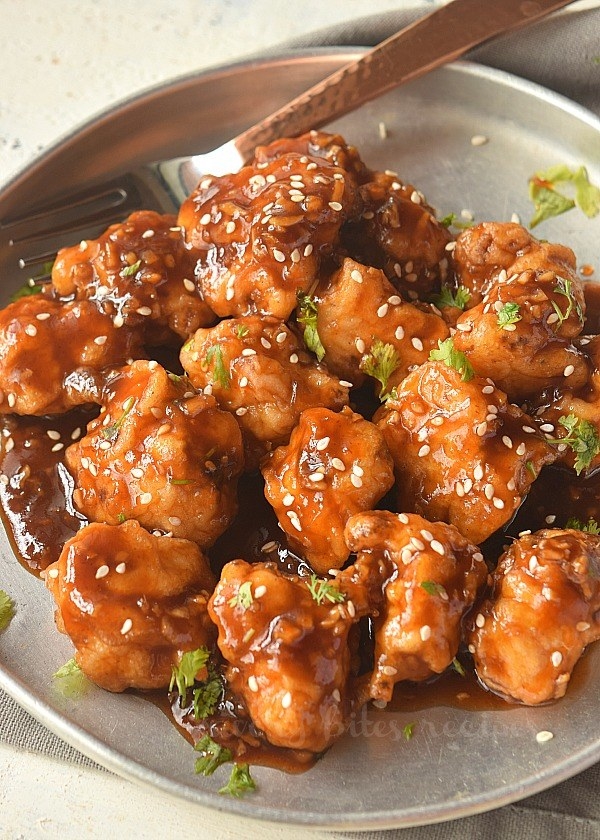 A plate of crispy, saucy General Tso&#x27;s cauliflower with sesame seeds and herbs.