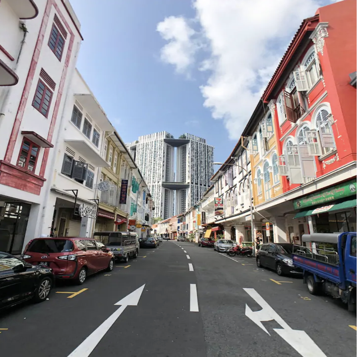 An empty street leads towards a large, modern looking building with colorful buildings lining the street
