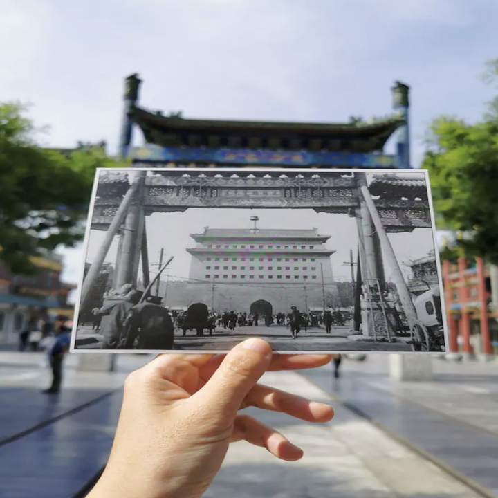 A hand holds up a black and white photo of a gate that perfectly fits into the real life background 