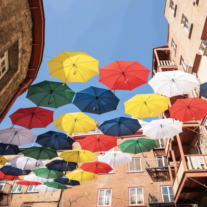 An upwards shot of colorful, open umbrellas hanging from building to building on a street