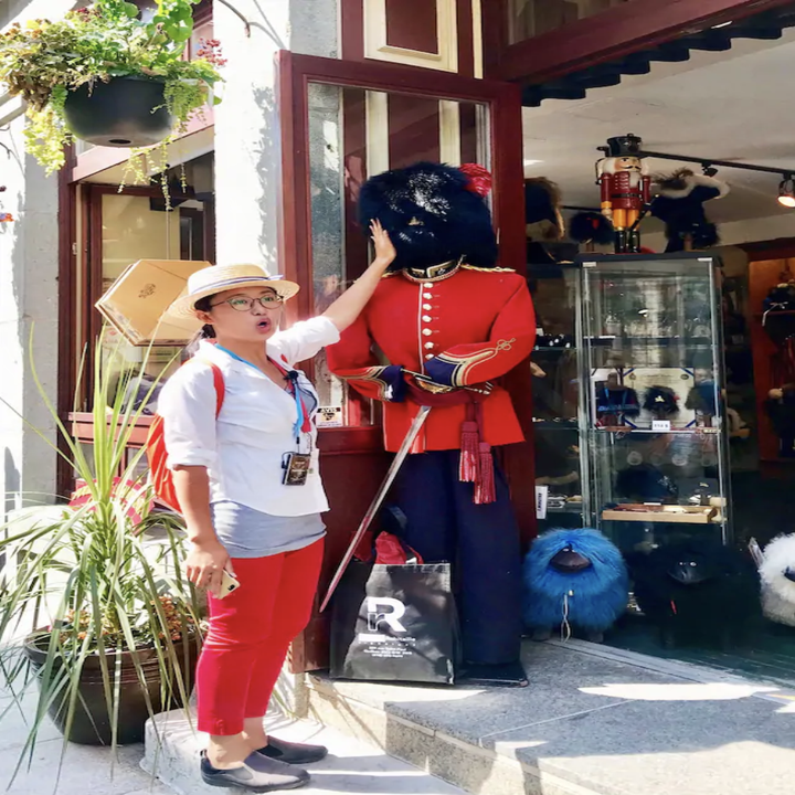 A woman makes a silly face at the camera as she places a hand on a novelty statue of an old fashioned guard costume