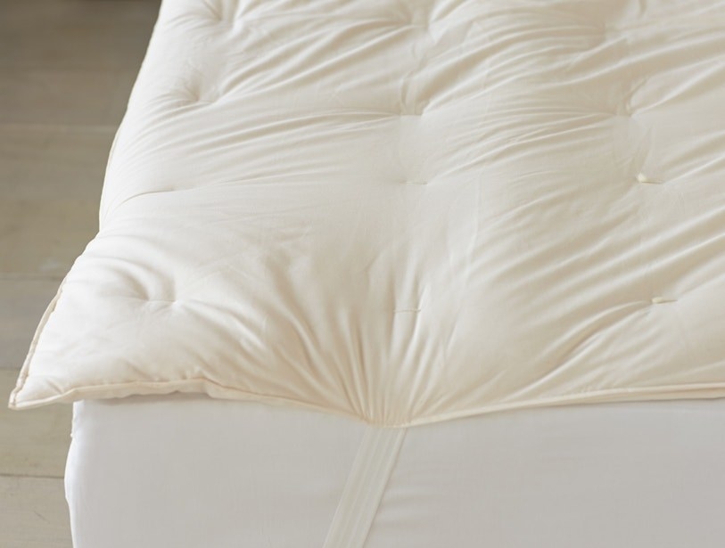 The off-white topper on a bed, secured under the mattress by elastic corner straps