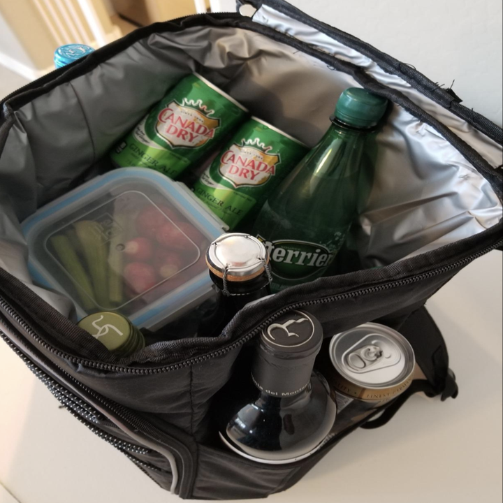 The cooler open with veggies and cans inside of it