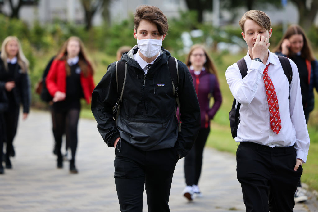 A high school boy wears a mask as he walks into school with his mask-less classmates
