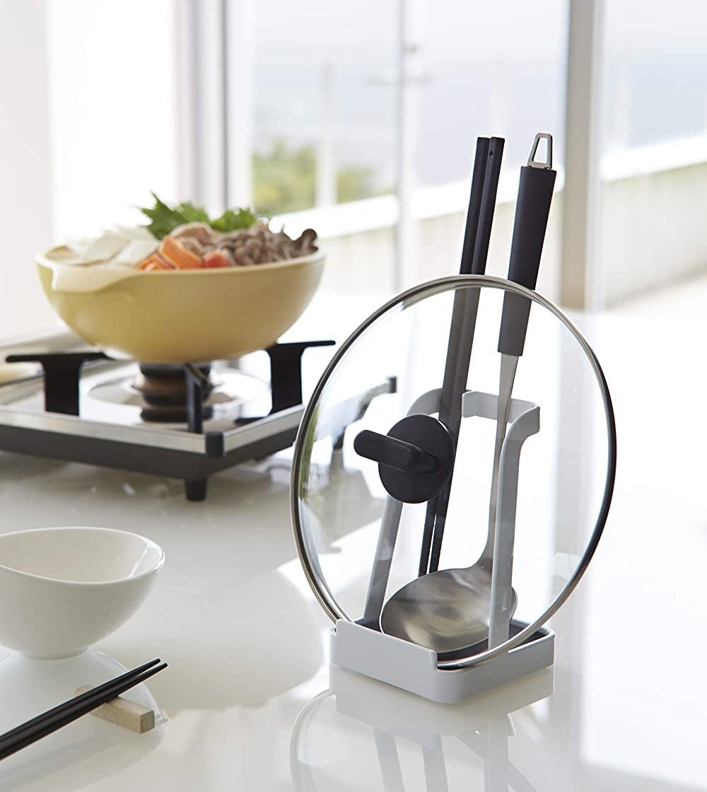 The stand holding a pot lid and a soup ladle on a clean countertop