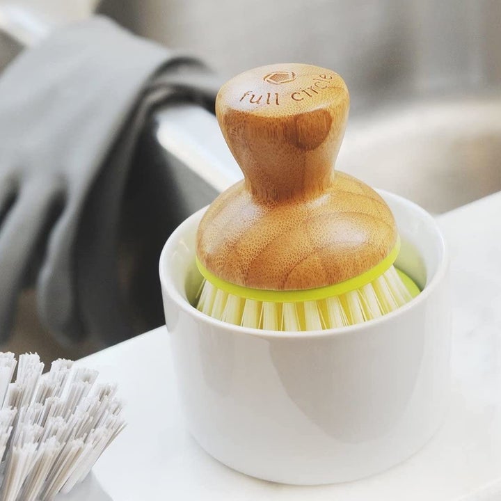 A close up of the brush and container set next to a sink