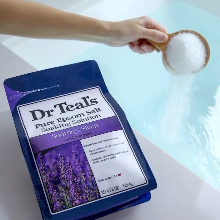 A person pours a cup of Epsom salts into a bath