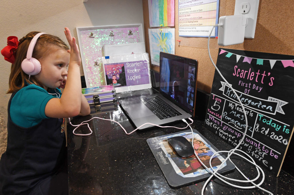 A little girl distance learning over the computer raises her hand during class