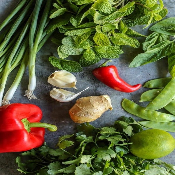 Ingredients on a table including scallions, cilantro, mint, pepper, garlic, ginger, and snap peas.