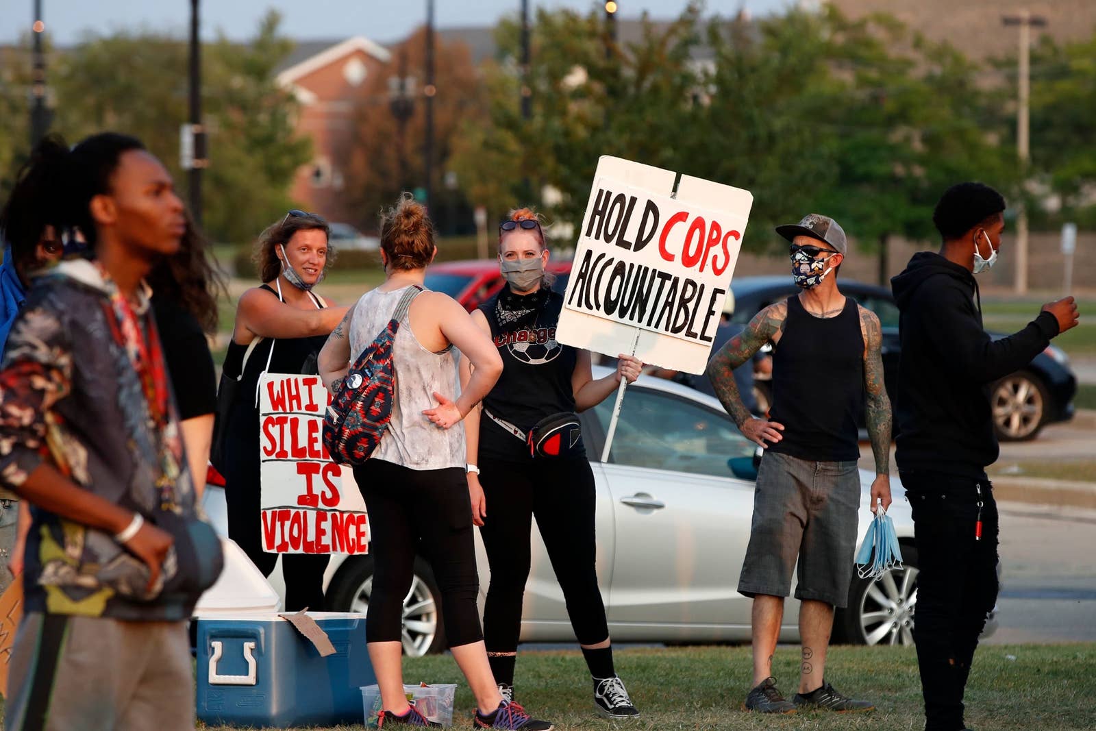 A white woman in a small group holds a sign saying &quot;hold cops accountable&quot;