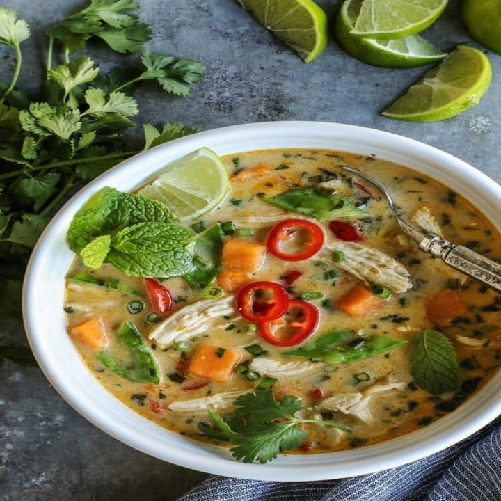 A bowl of Thai coconut chicken soup with peppers, herbs, shredded chicken, and sweet potato.