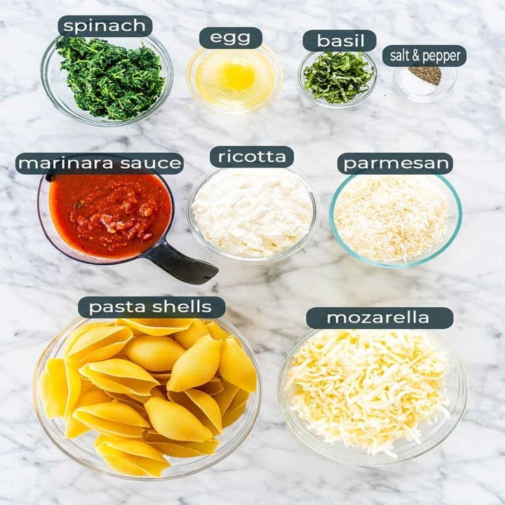 Ingredients for stuffed shells like spinach, egg, basil, marinara sauce, cheese, and pasta shells.