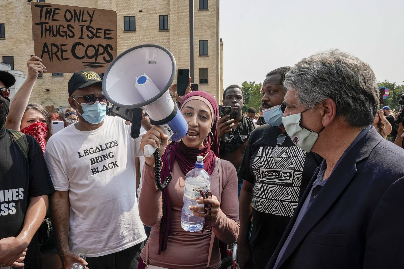 A woman with a pink hijab speaks on a megaphone amidst a crowd 