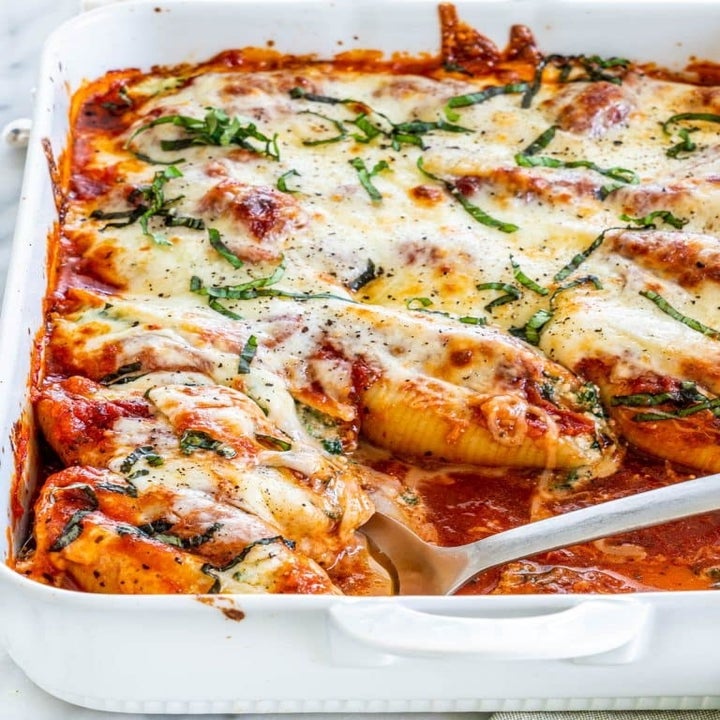 A baking dish filled with spinach and cheese stuffed shells, topped with a layer of cheese, marinara sauce, and basil.