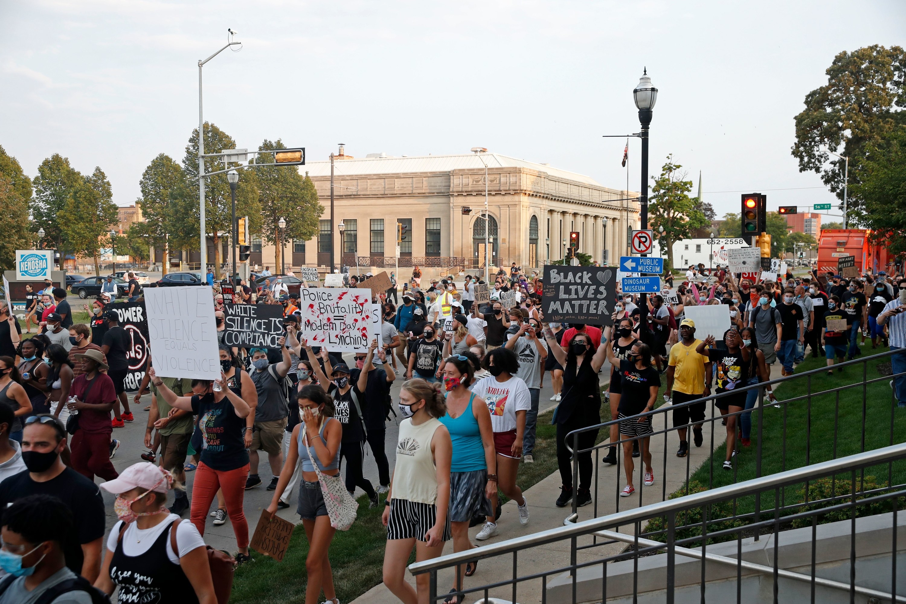 A large crowd of people walk down the street in the afternoon with signs