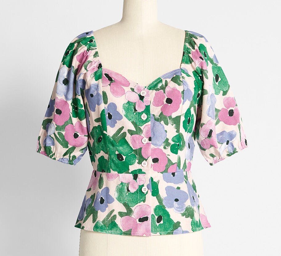 The blouse with puff sleeves, sweetheart neckline, and buttons down the front with a pink, purple, and green floral print all over