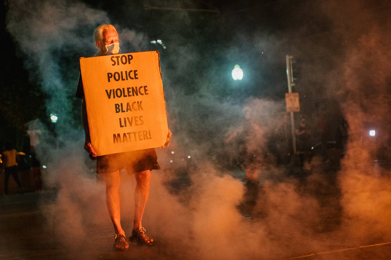 A man stands with a sign reading &quot;stop police violence, black lives matter&quot;