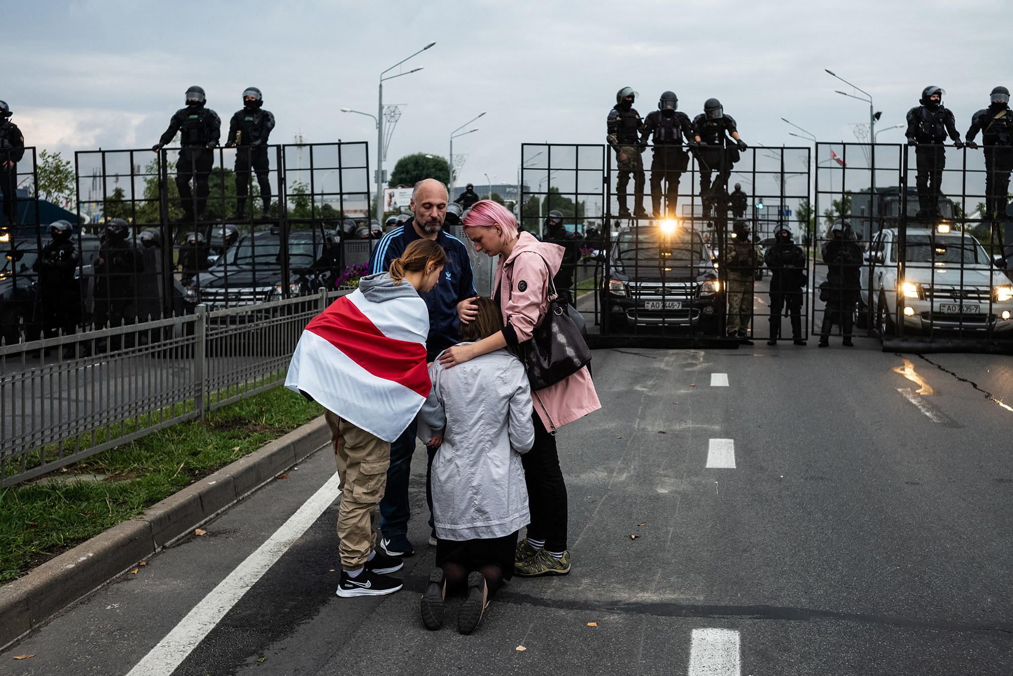 Protesters are consoling a woman as police look on from behind a fence