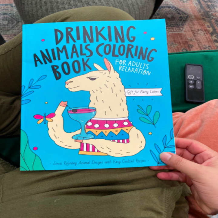 Reviewer holds colorful book that says "Drinking Animals Coloring Book" while sitting on a couch