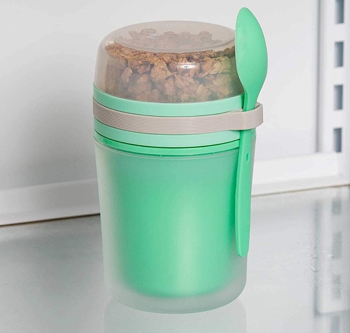 the green container with an attached green spoon and clear top compartment 