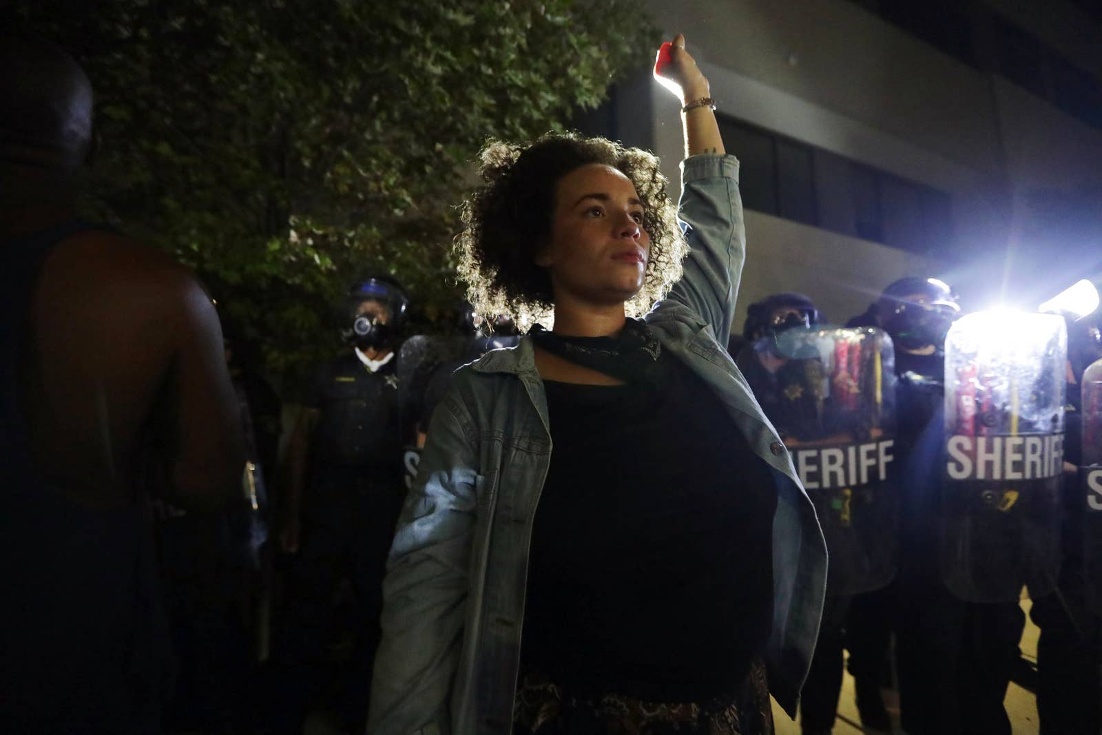 A woman holds her fist up in the air in front of a crowd of police