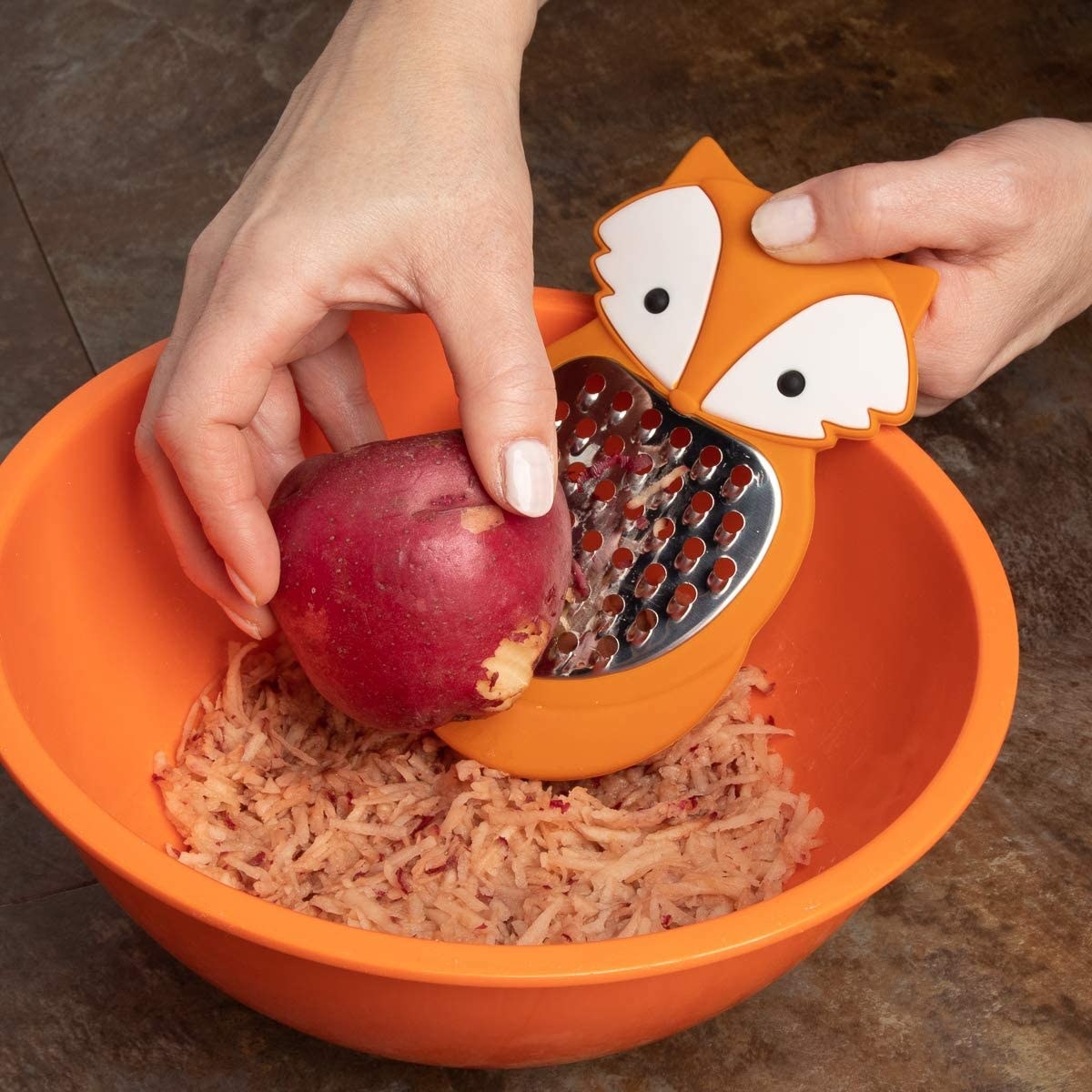 A person grating an apple into a bowl with a small grater with a fox face on the handle