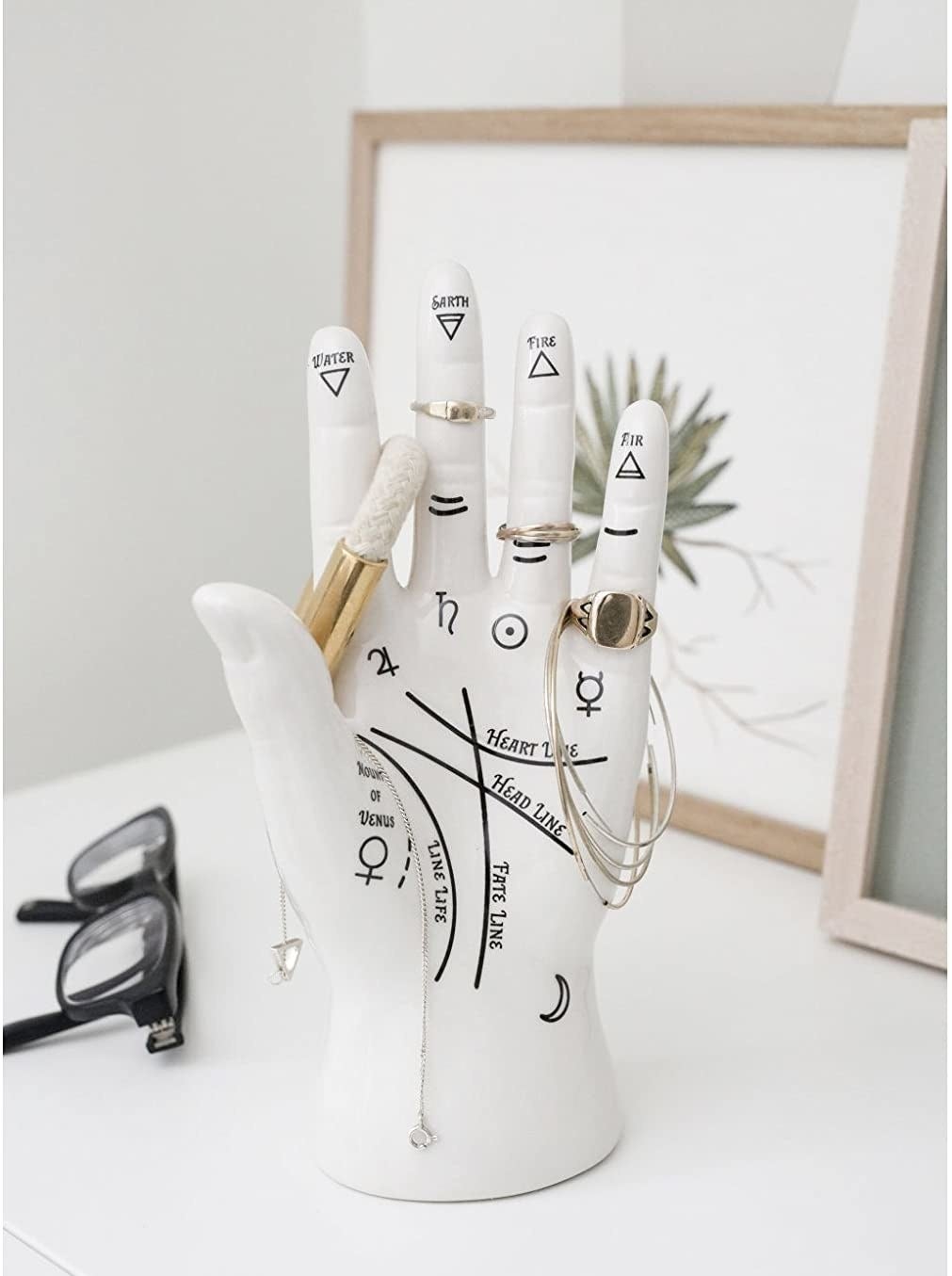 The palm-shaped jewelry stand on a vanity, holding rings, necklaces, and other jewelry