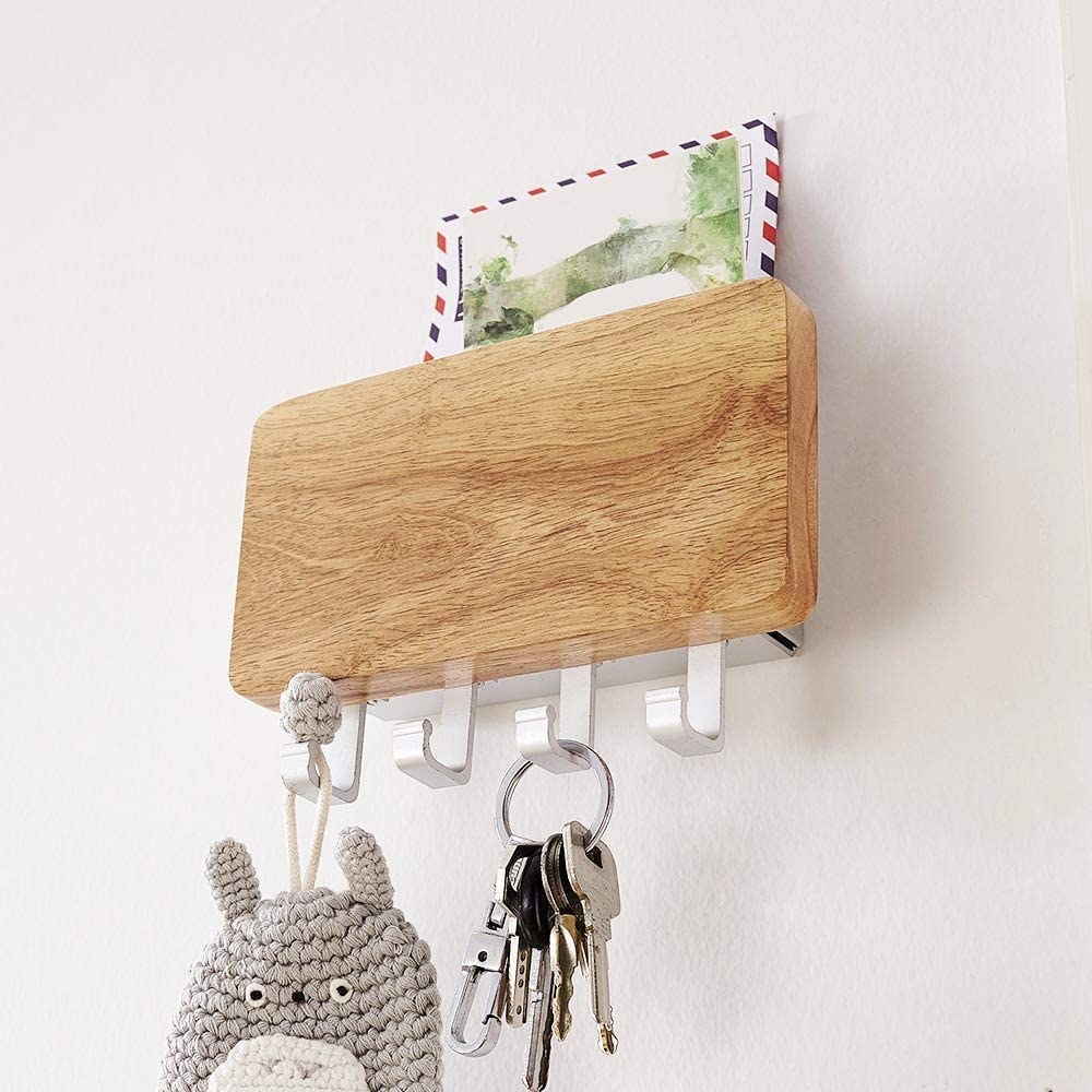 The key holder mounted on a wall, containing one envelope, one set of keys, and a knitted key chain