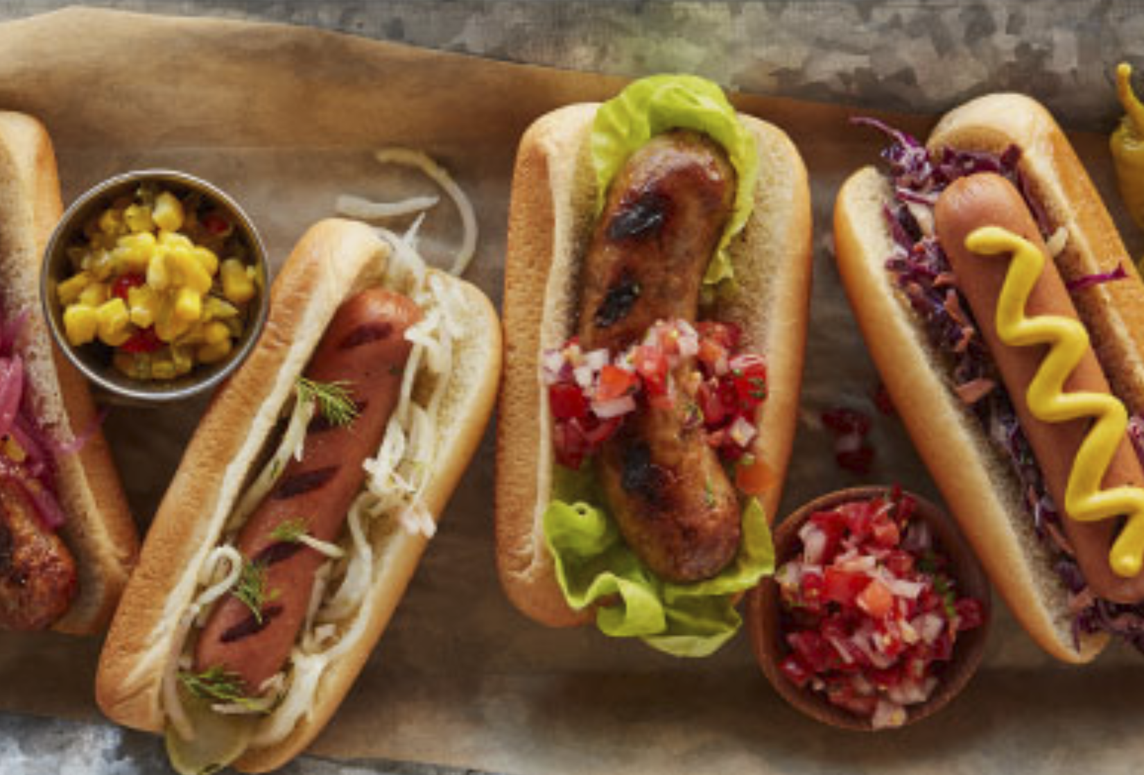 Hot dogs in buns with different toppings like lettuce, rosemary, mustard, purple cabbage, corn, and more. These are, um, creative options.