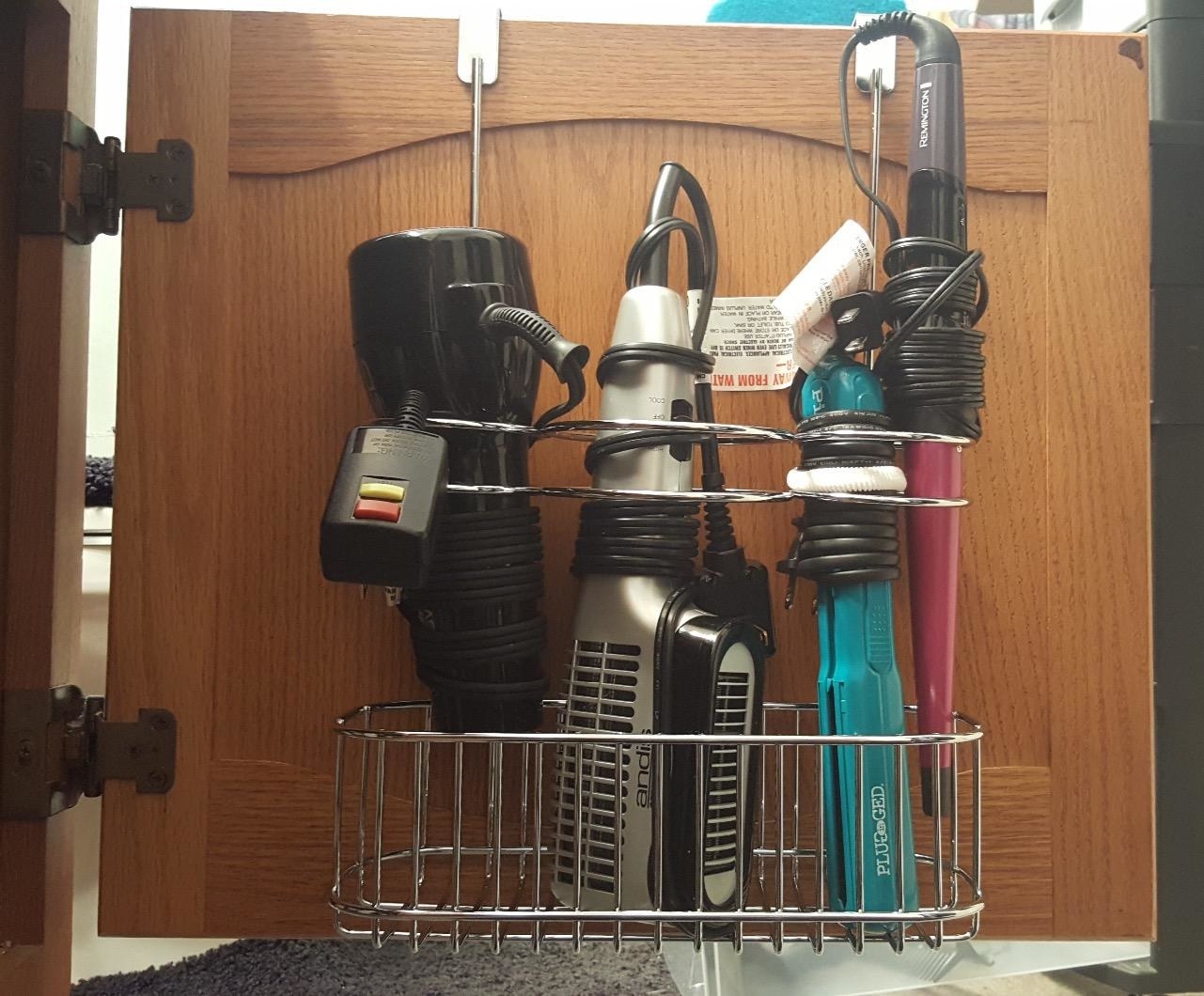 A reviewer&#x27;s organizer on the back of their cabinet, with two compact hair dryers, a straightener, and a curling iron