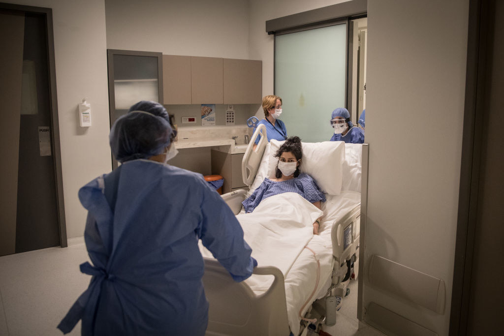 戴面罩的妇女坐在医院准备分娩的床上