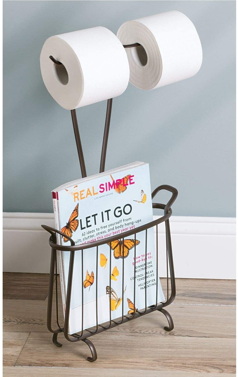 The bronze iDesign Axis Free Standing Toilet Paper Holder and Newspaper and Magazine Rack holding two rolls of toilet paper and a magazine