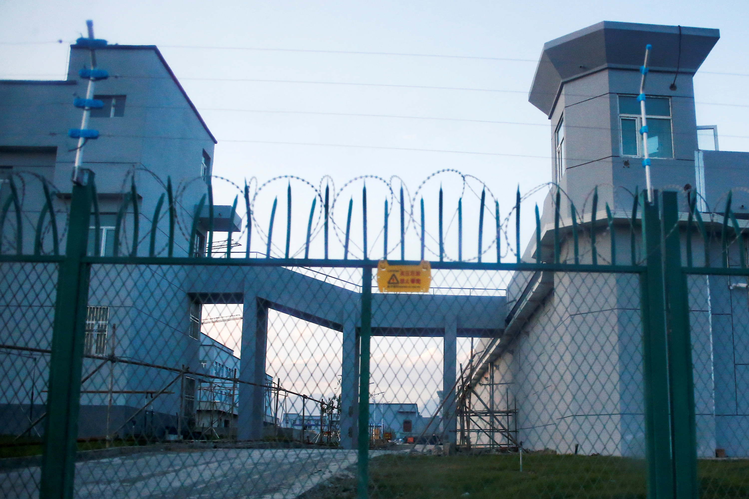 Barbed wire lines the top of a spiked fence in front of a large prisonlike complex