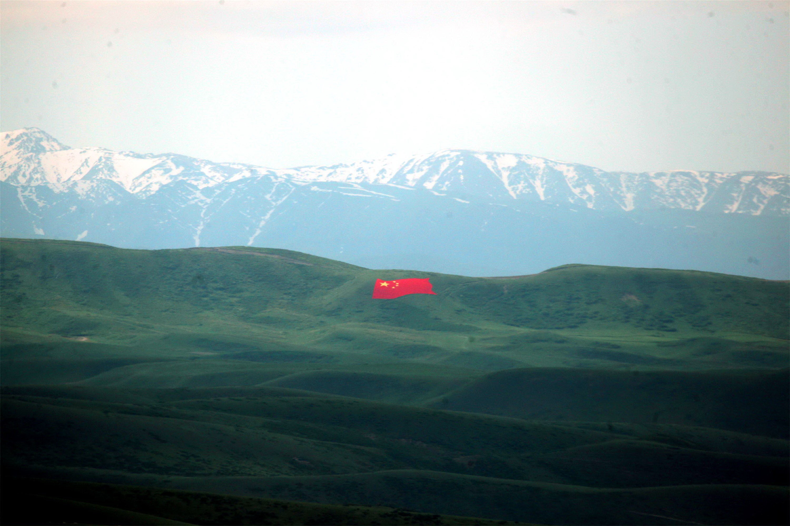 A massive Chinese flag which has been painted on a hill, with a large mountain range in the background