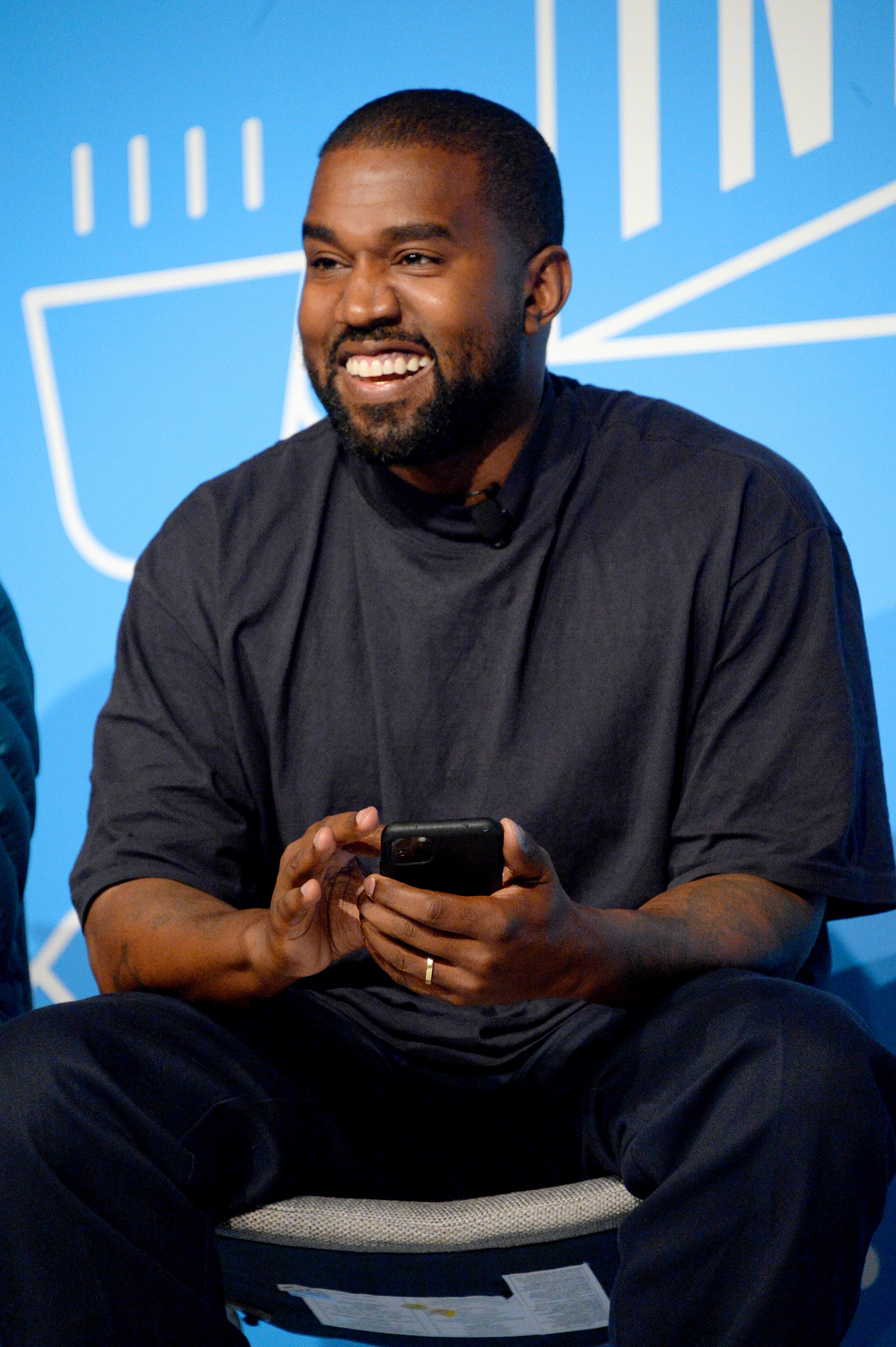 Kanye West smiles with his phone in his hand