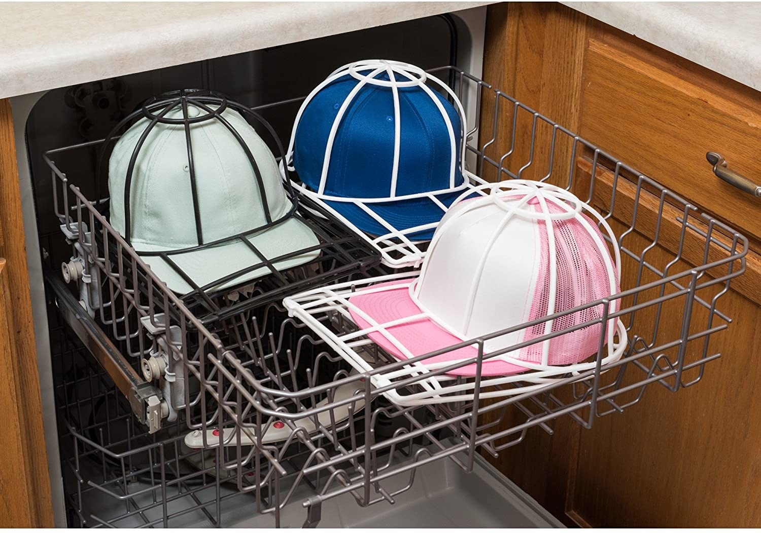 Three baseball caps in protective plastic cages sitting on the top rack of a dishwasher