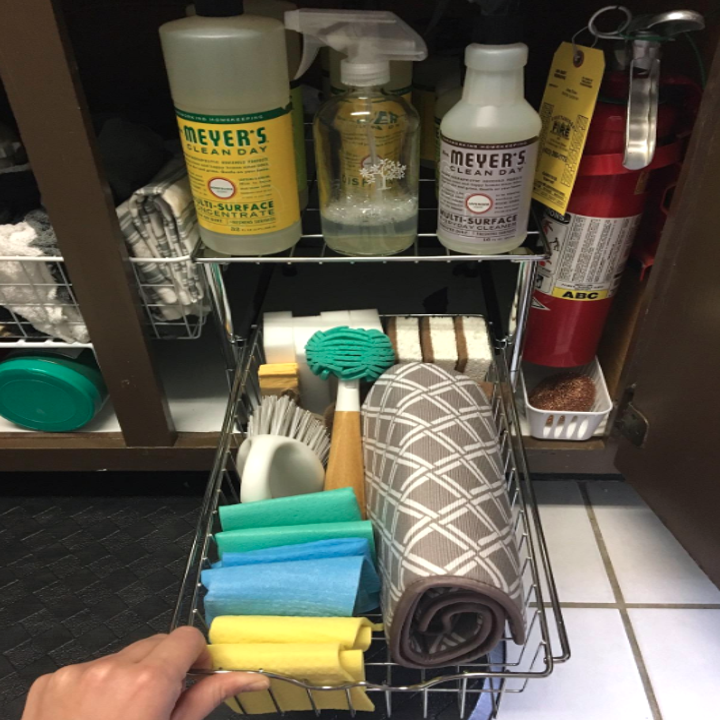 A reviewer pulls out their drawer to reveal three sponges, four magic erasers, two handheld scrub brushes, one dish brush, four folded dish cloths, and a folded drying pad all neatly arranged