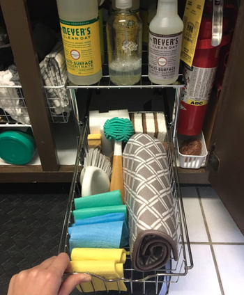 A reviewer pulls out their drawer to reveal three sponges, four magic erasers, two handheld scrub brushes, one dish brush, four folded dish cloths, and a folded drying pad all neatly arranged