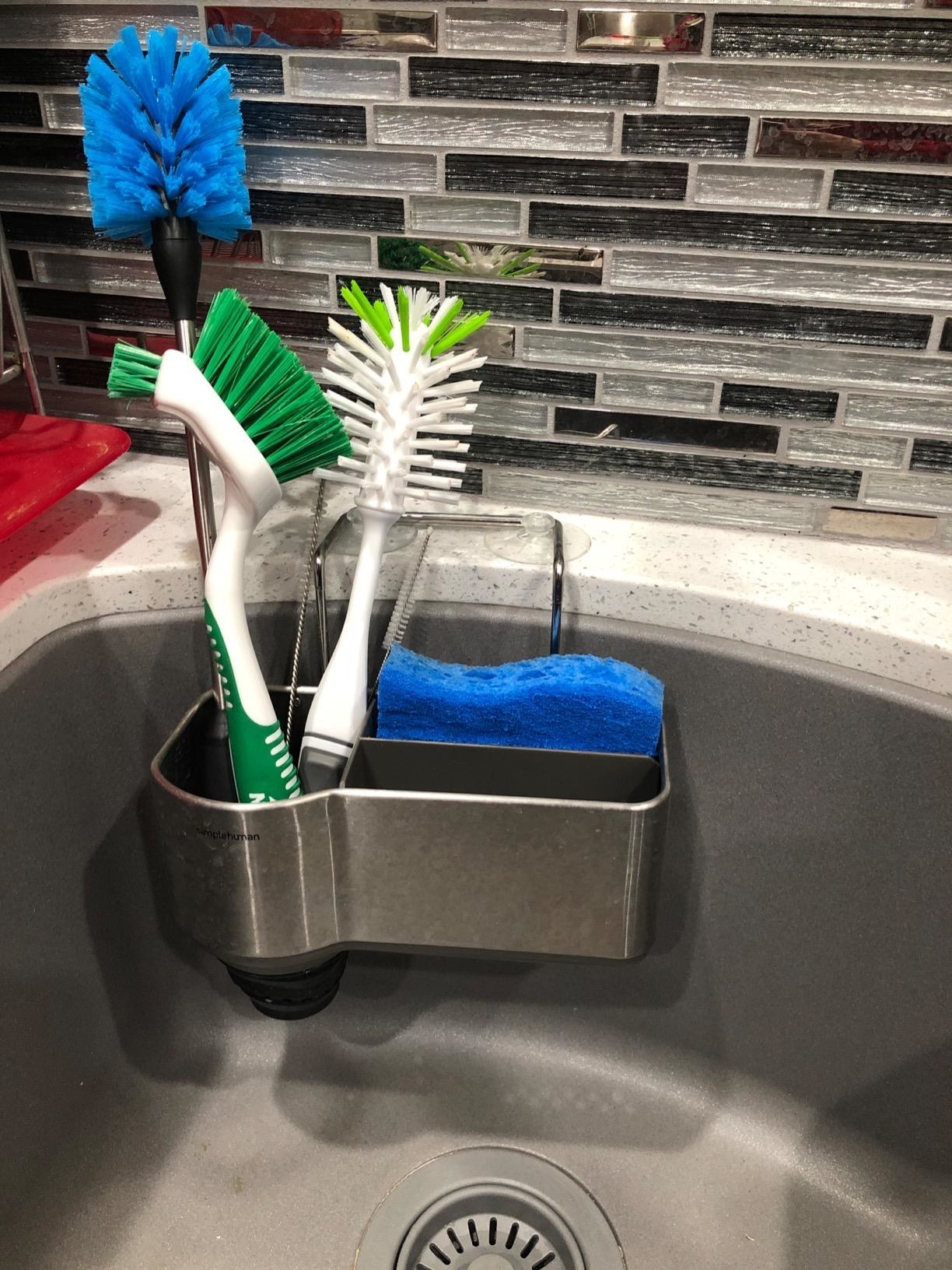 Sink caddy attached to the side of a sink with brushes and sponge inside