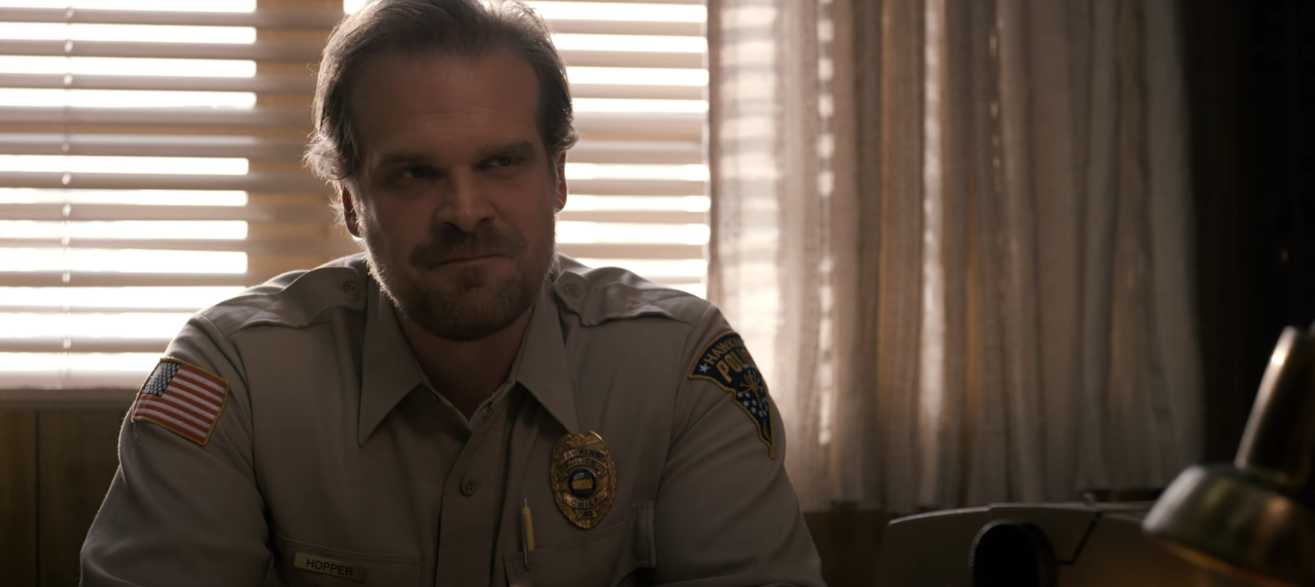 Hopper sits at his police chief desk while wearing the uniform in &quot;Stranger Things.&quot; 