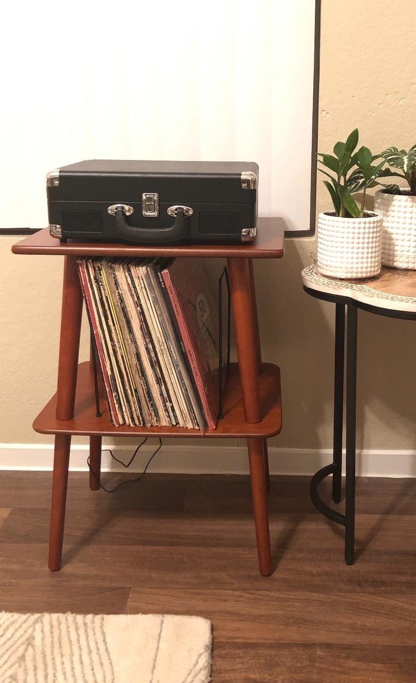 Reviewer pic of the brown wood two-tier stand with black wire slots in the middle holding vinyl records and a record player on top