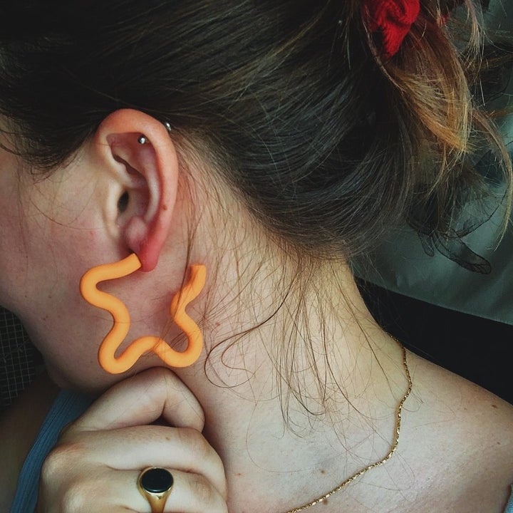 a model wearing orange hope earrings that have a wavy design
