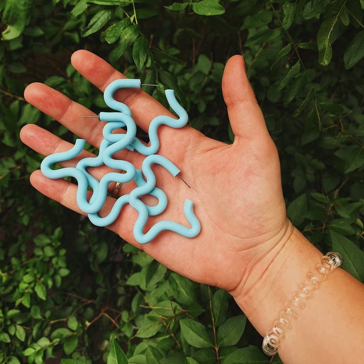 model's hand holding four blue versions of the earring